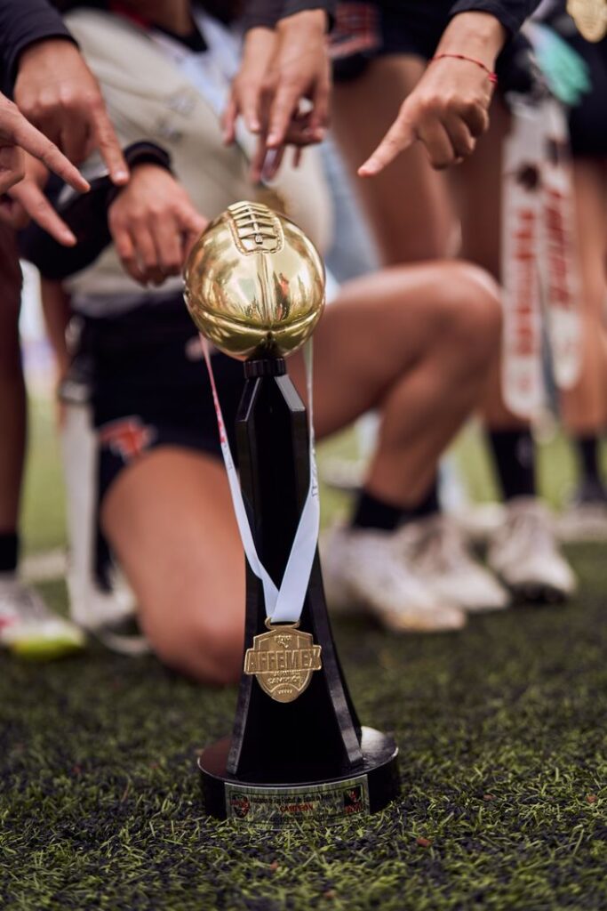 A victorious team celebrates with a gold football trophy on the field.